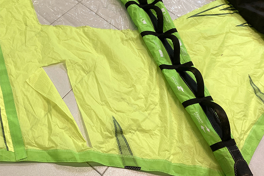 Imagen de un wing foil de color amarillo y verde con un descosido en la parte izquierda que va a ser reparado