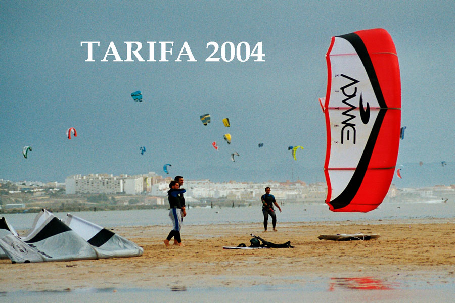 Tres personas equipadas para practicar Kitesurf en la playa de Tarifa desplegando una cometa de Kite Surf de color rojo y blanco